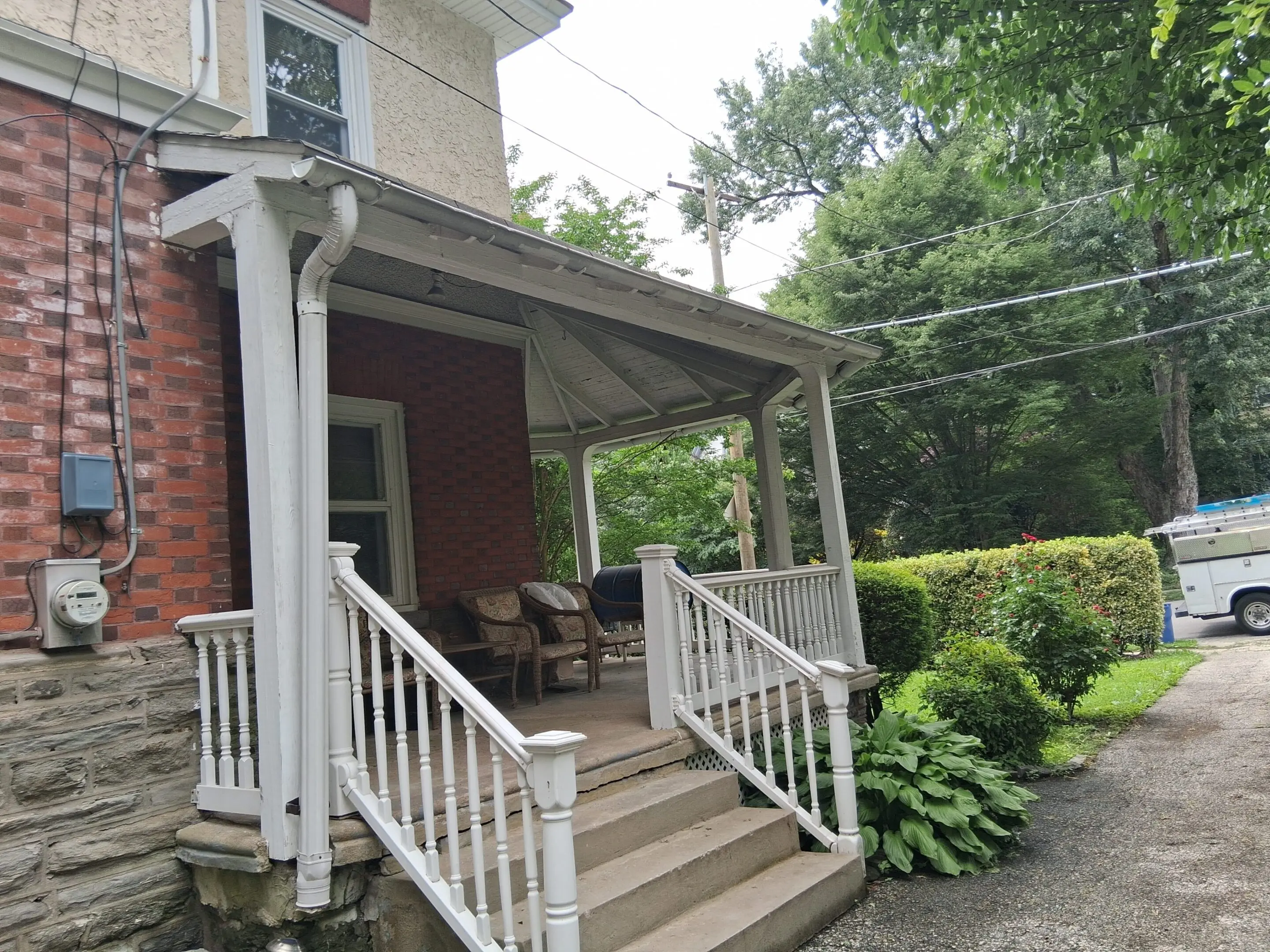 Cozy porch with white railings and wooden steps on a brick house.