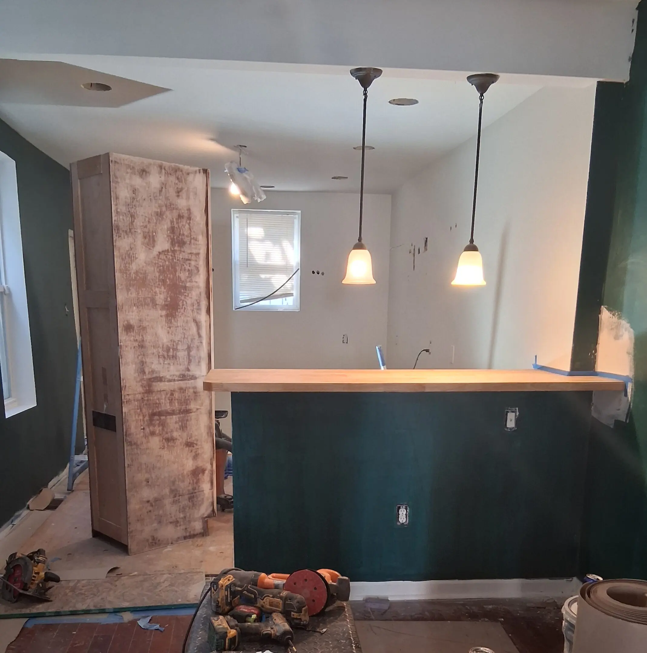 Home bar area under renovation with pendant lights and a wooden countertop.