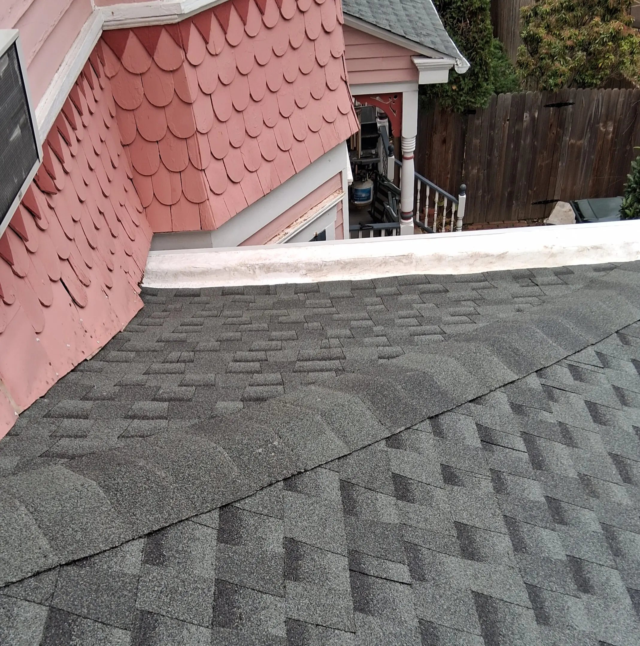 A roof with overlapping gray shingles and a pink wall with scalloped siding.