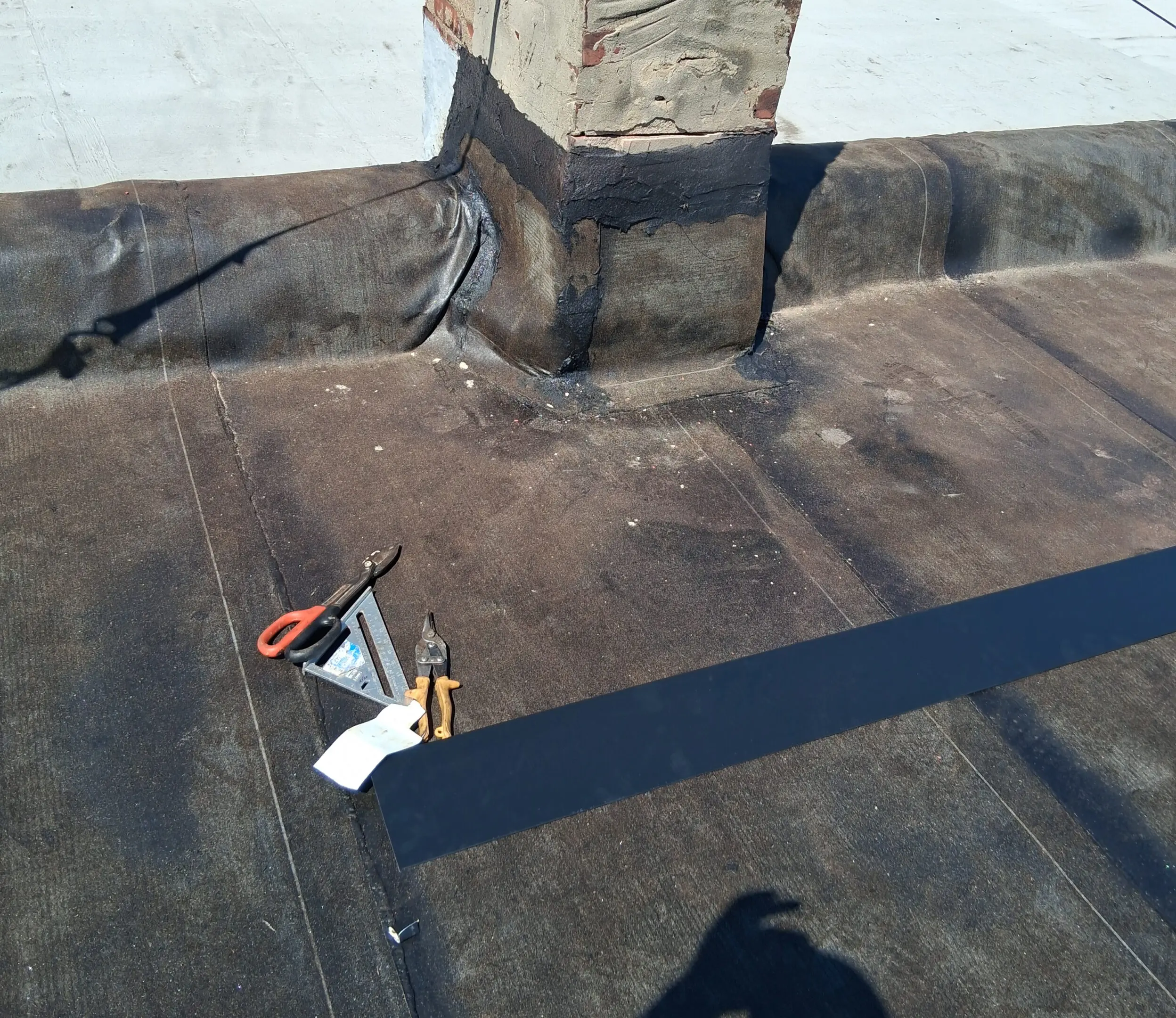 A person working on a flat roof with tools and a shadow visible.