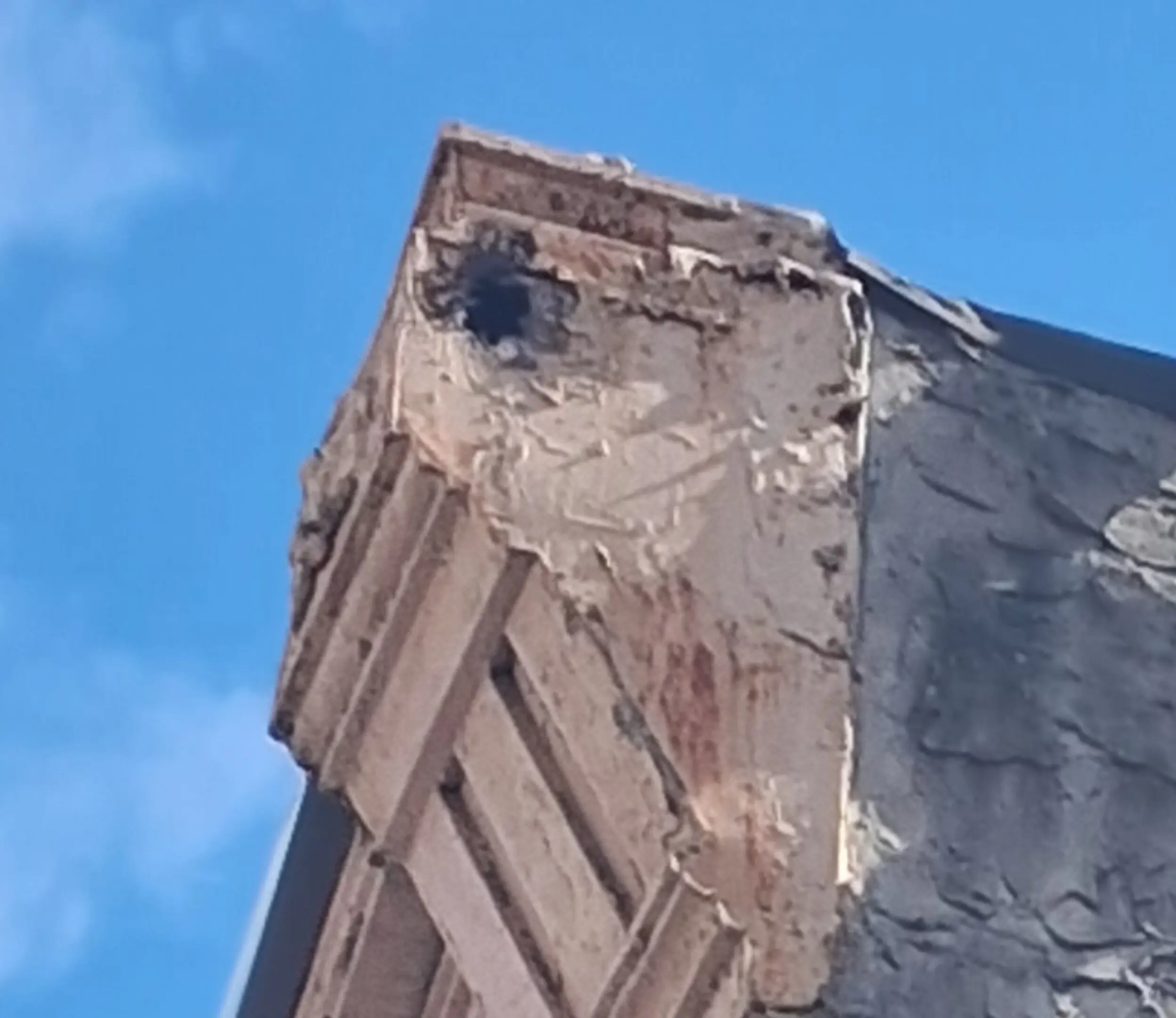 Damaged corner of an old building against a blue sky.