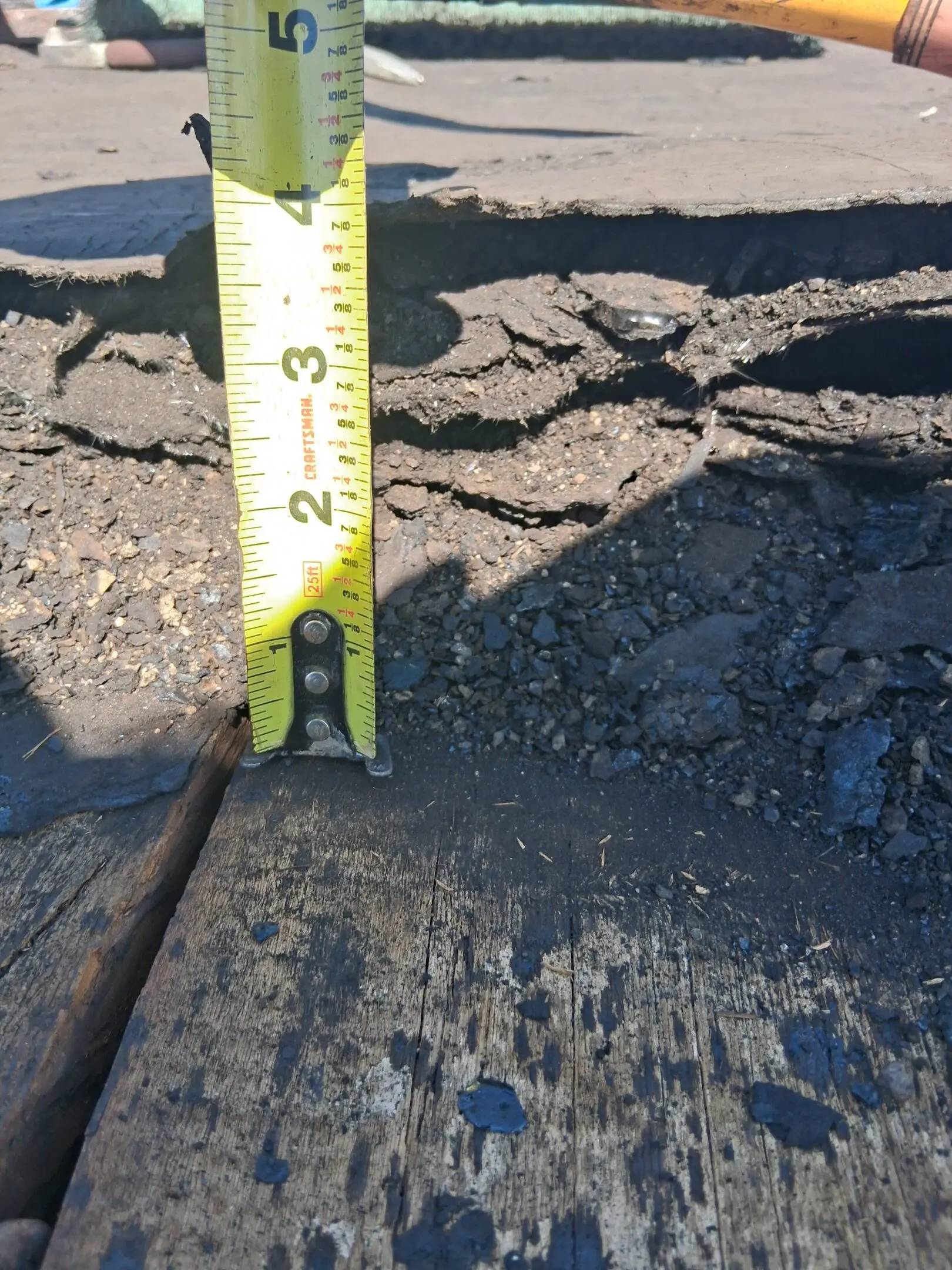 Close-up of cracked concrete with measuring tape showing depth.