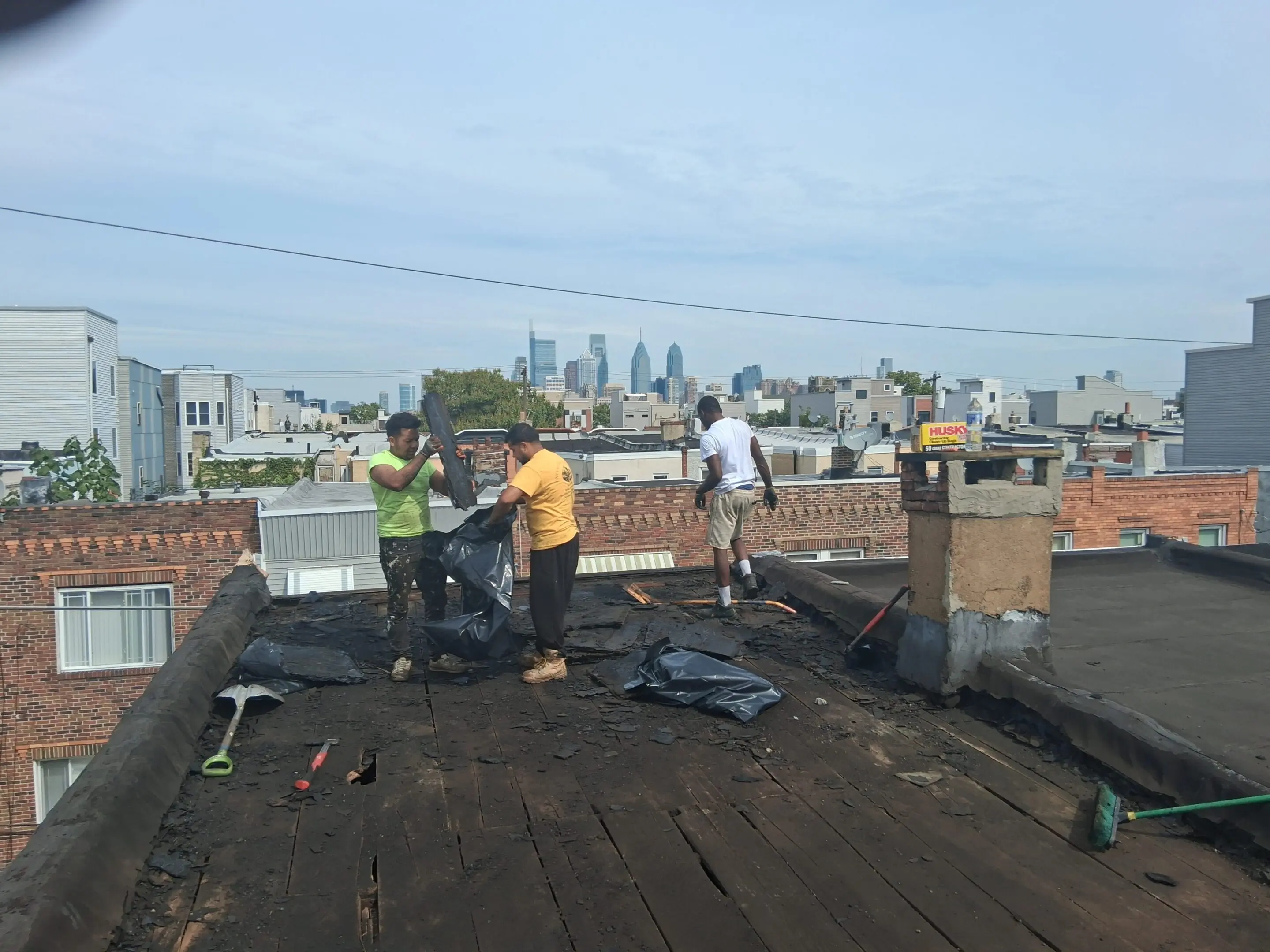 Workers repairing a rooftop with a city skyline in the background.