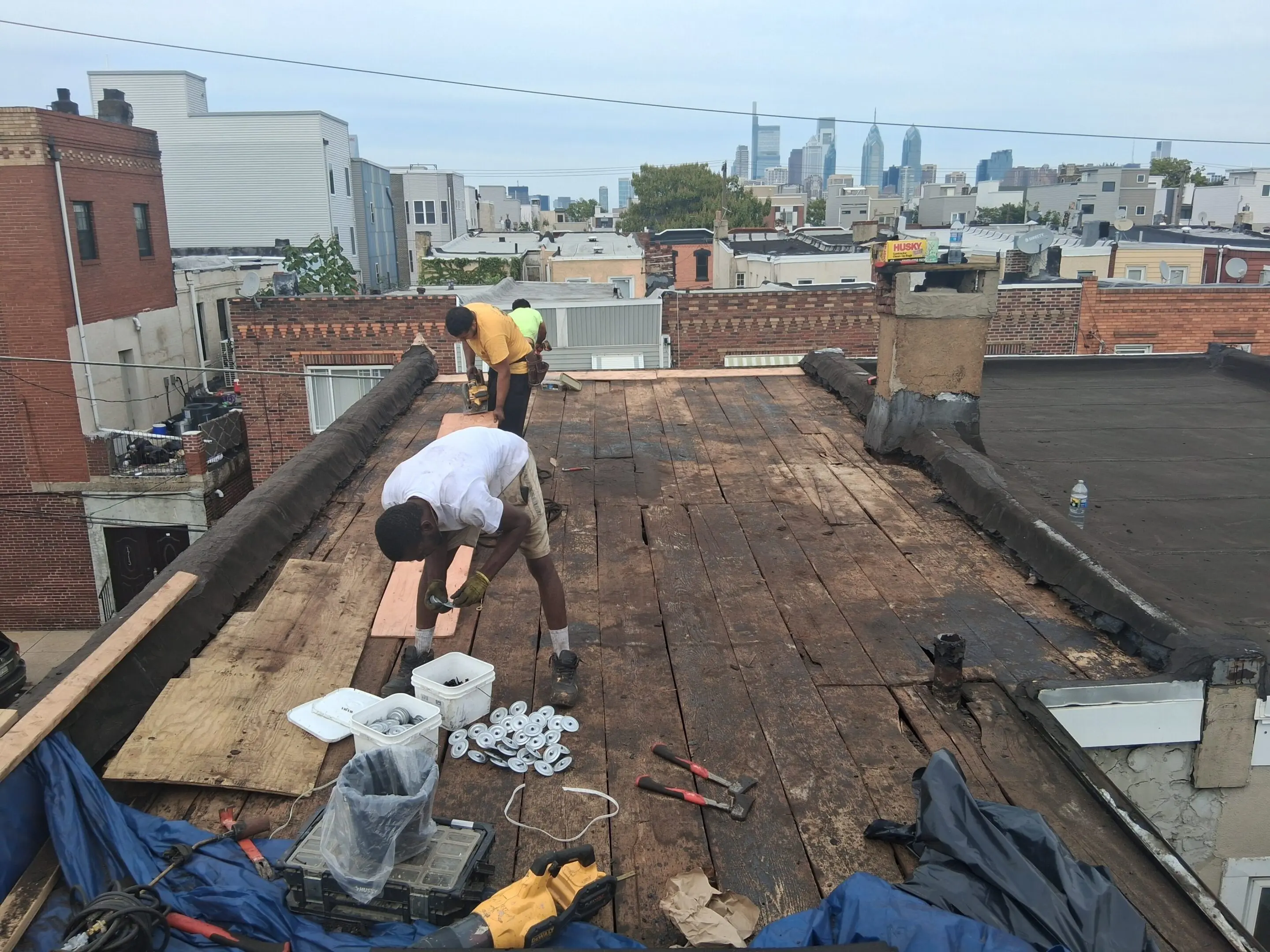 Workers repairing a rooftop with city skyline in the background.