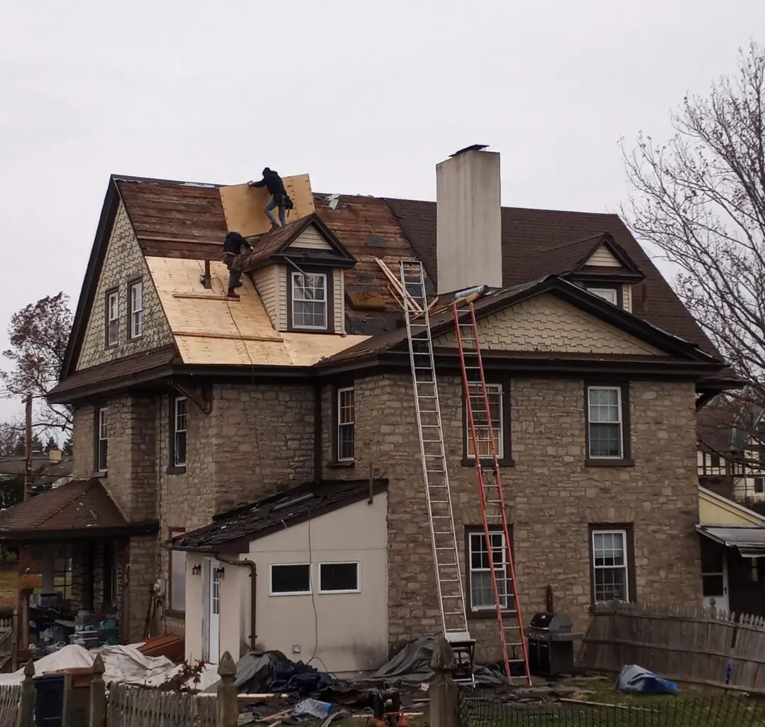 Workers repairing the roof of a large brick house.