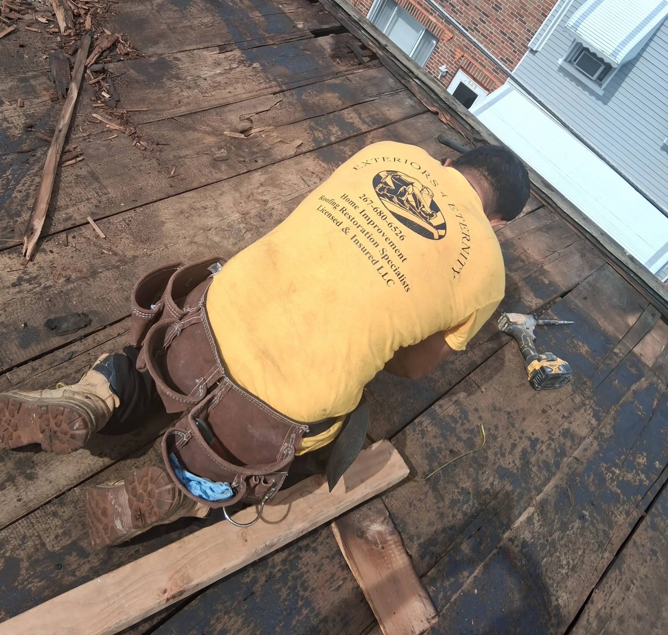 Worker in a yellow shirt installing roofing materials on a house.