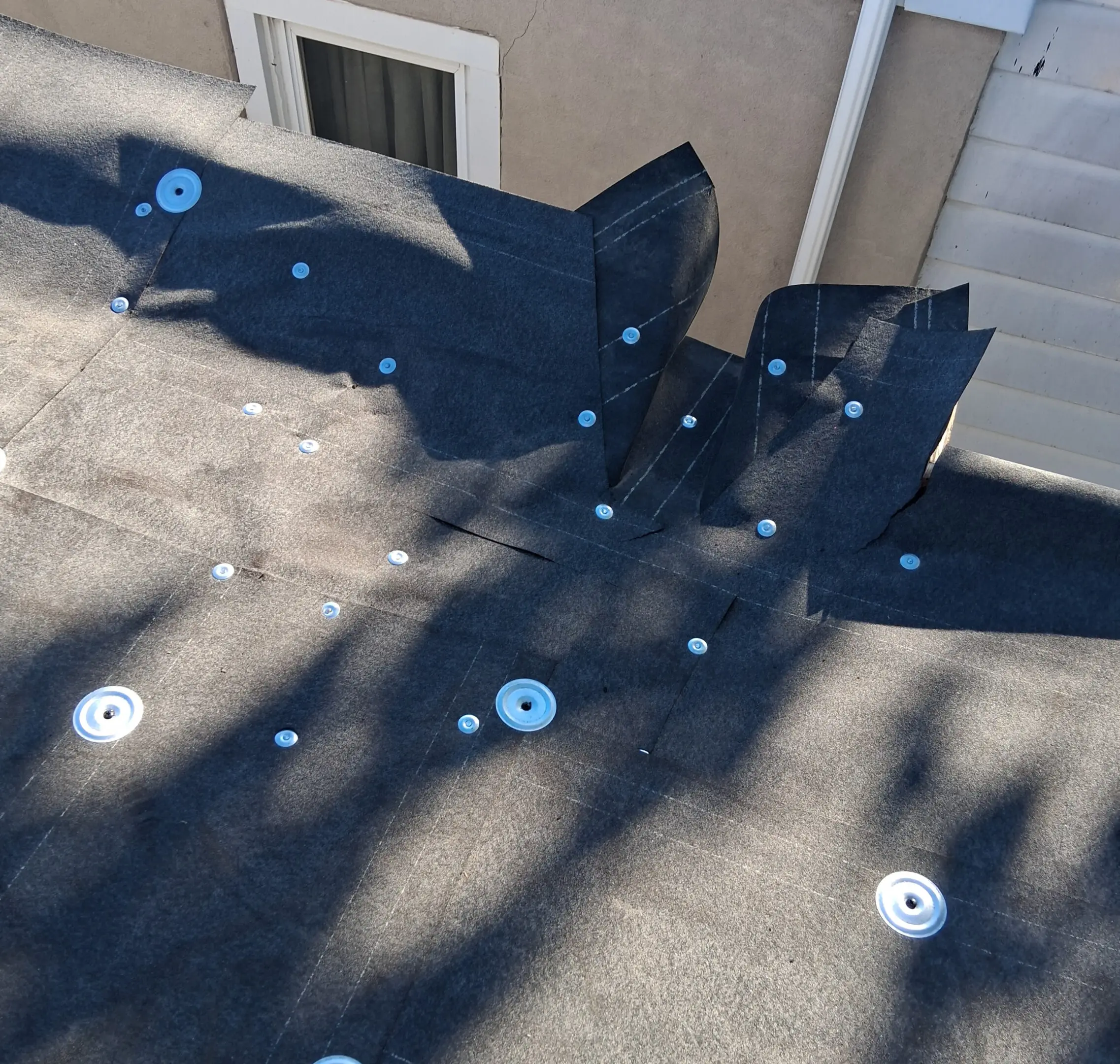 Black plastic roofing sheets laid out with washers on a roof under sunlight.