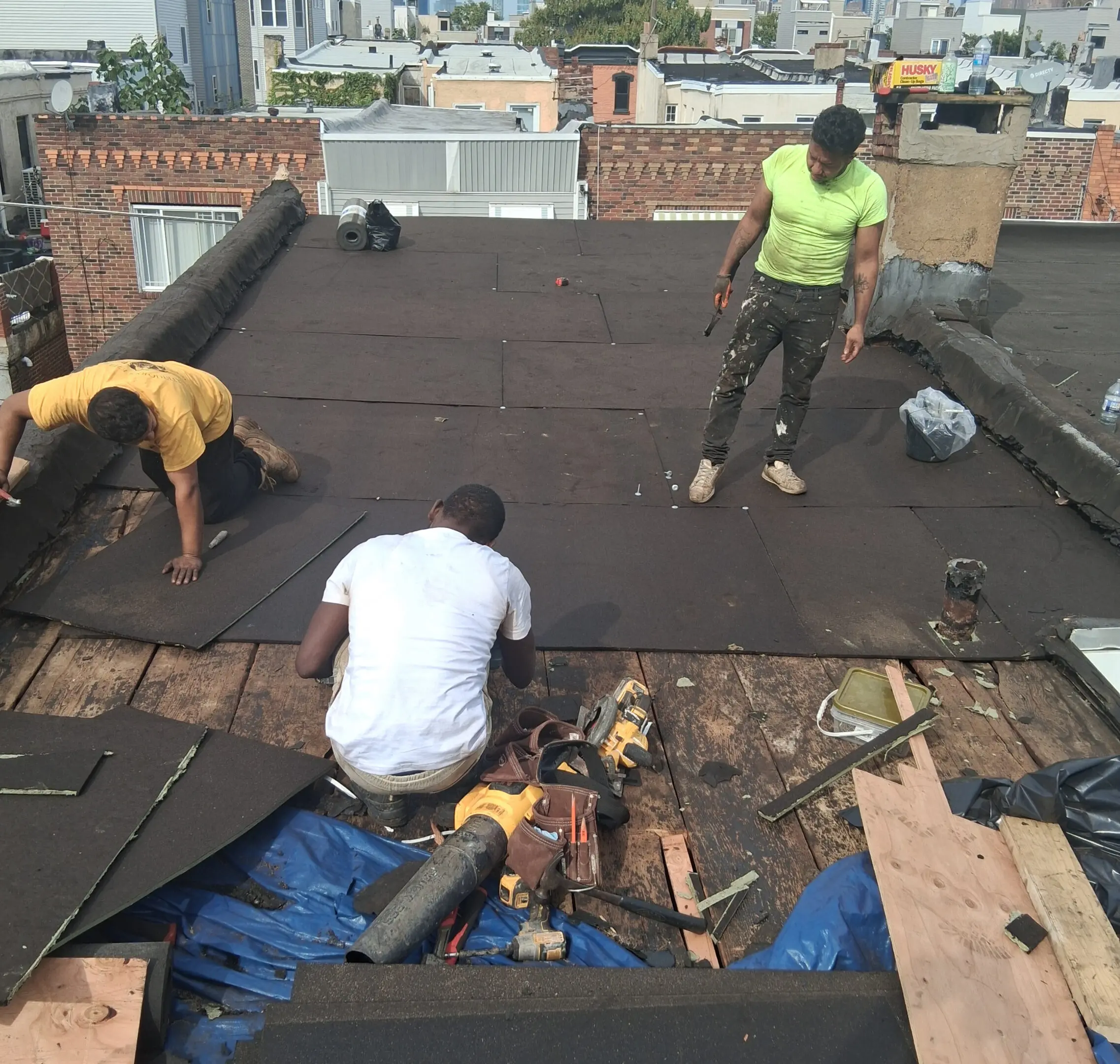 Three workers applying roofing material on a flat roof.