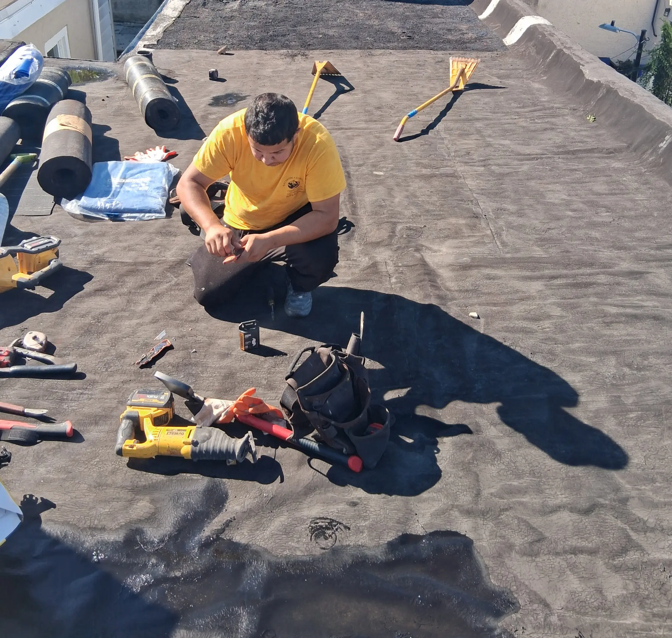 Worker in yellow shirt fixing equipment on a black surface outdoors.
