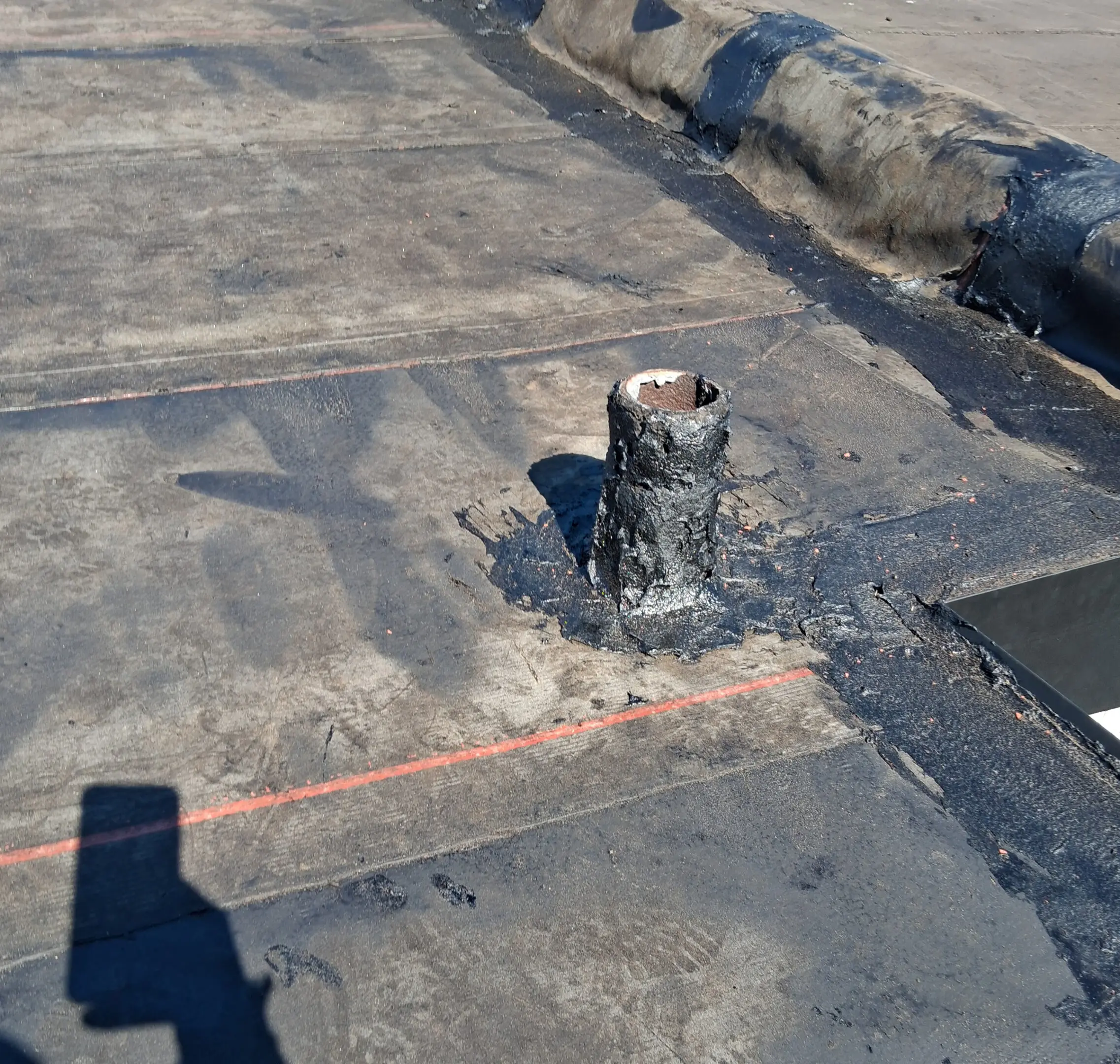 A rooftop with a vent pipe and a shadow of a person taking the photo.