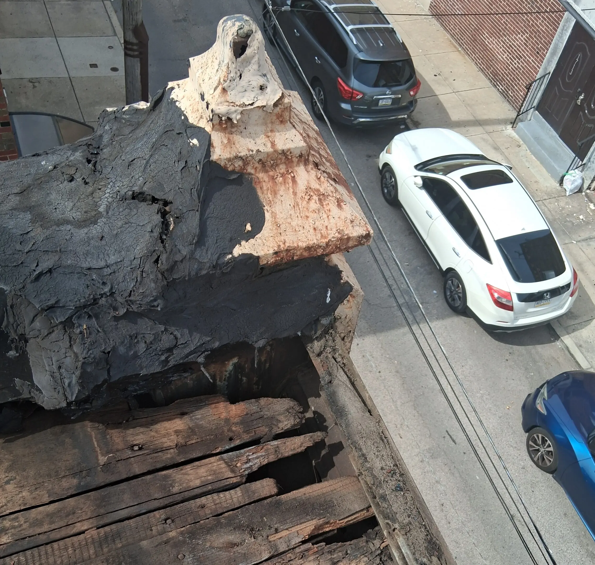 A large charred tree trunk section on a rooftop overlooking parked cars.