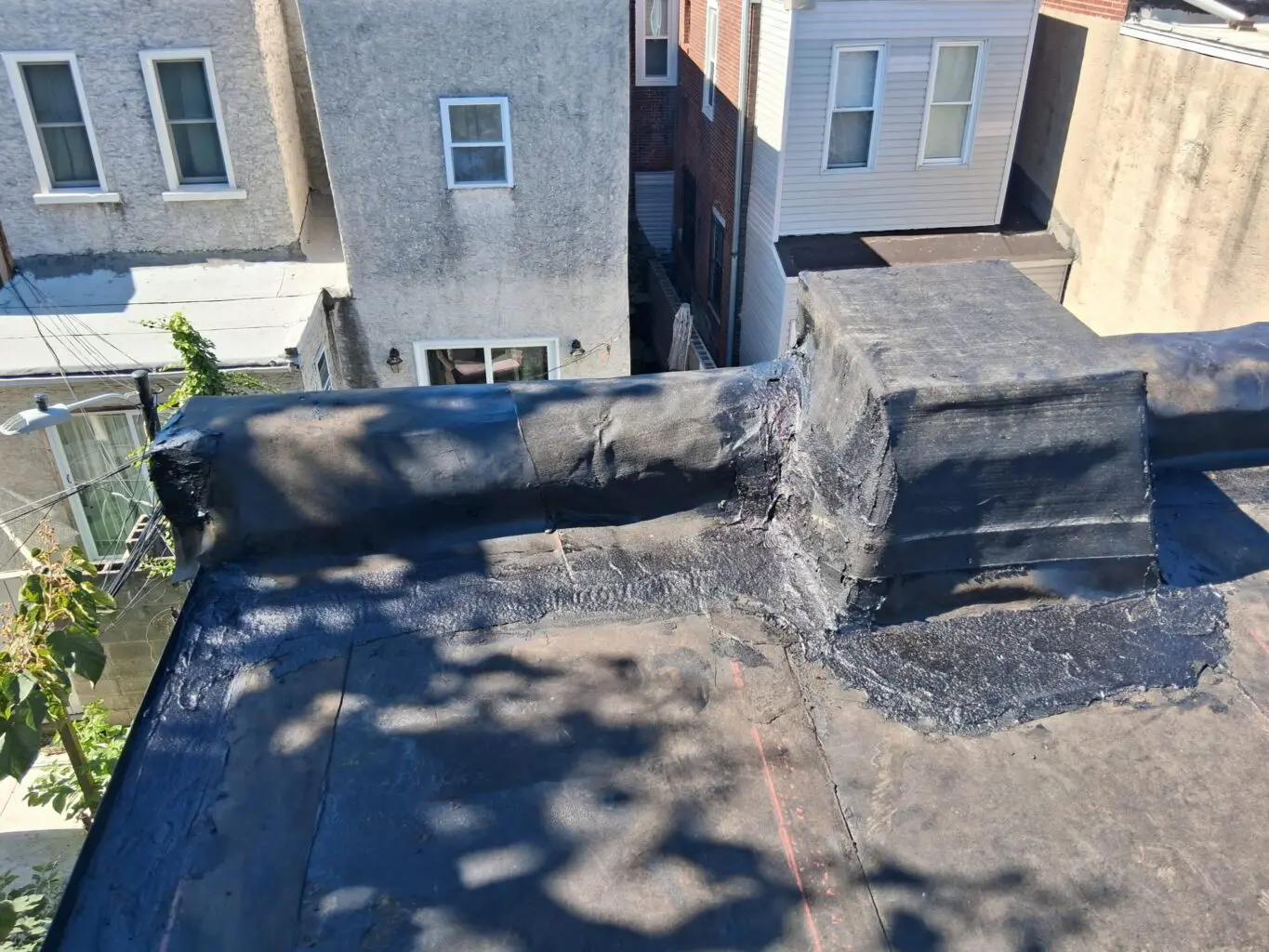 Flat rooftop with a chimney and shadows from nearby trees.