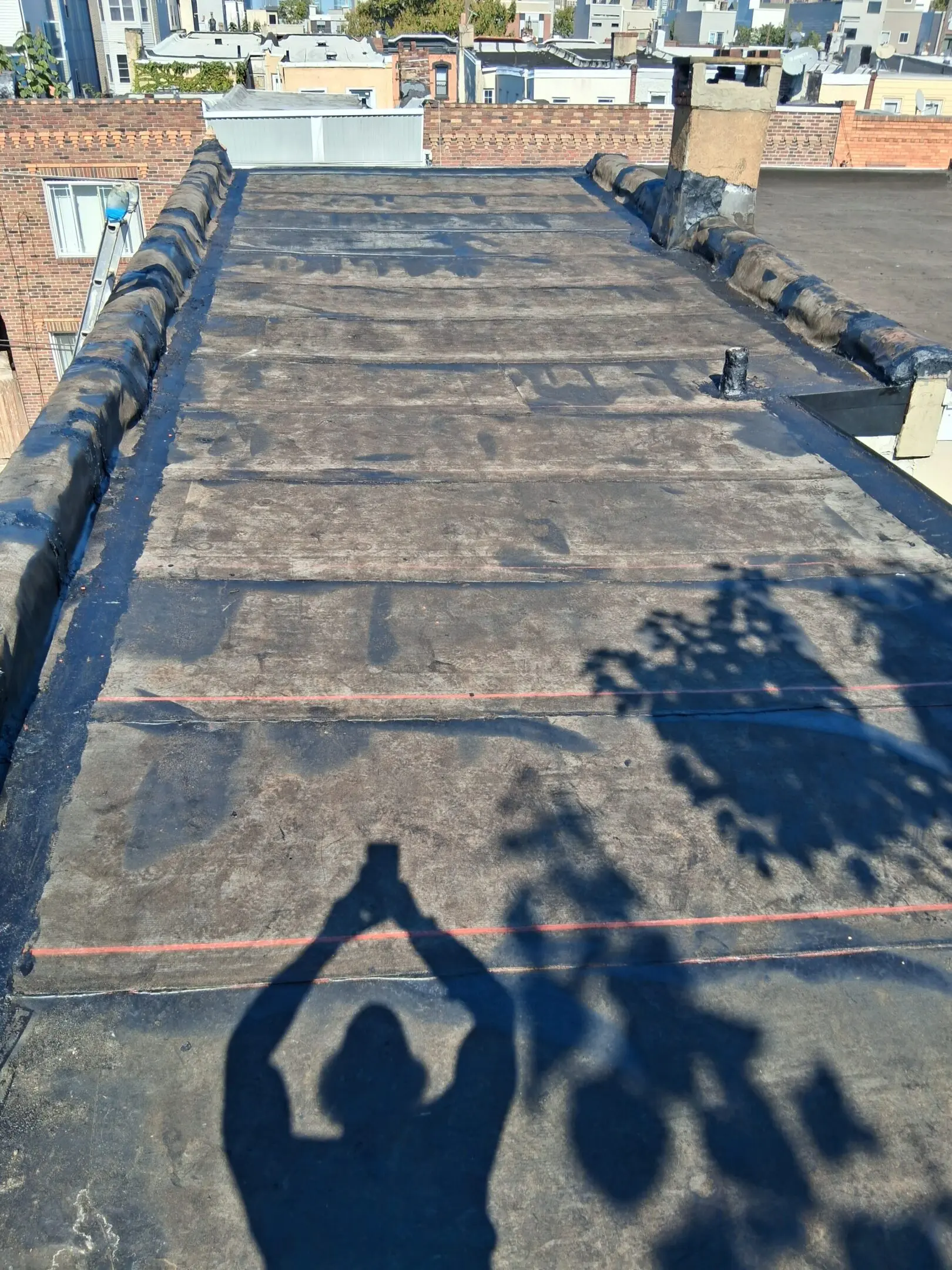 A rooftop covered with black waterproofing material under sunlight.