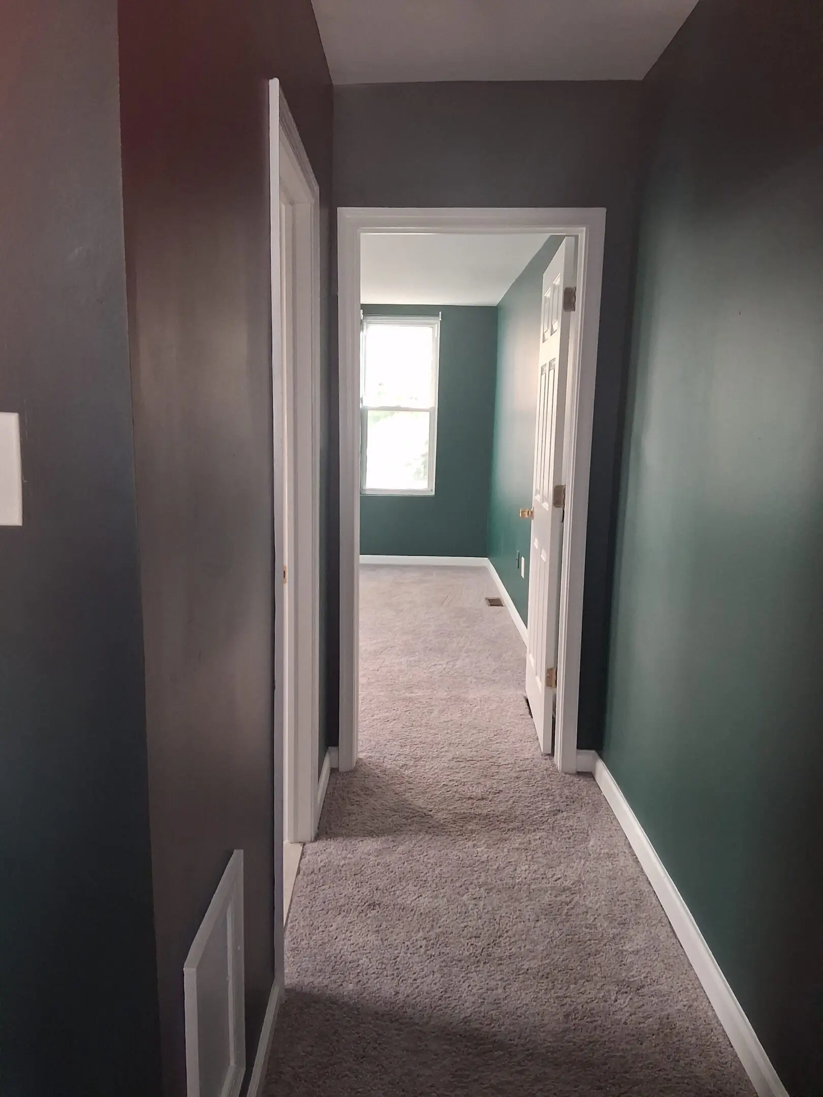 View of a carpeted hallway leading to a window-lit room.