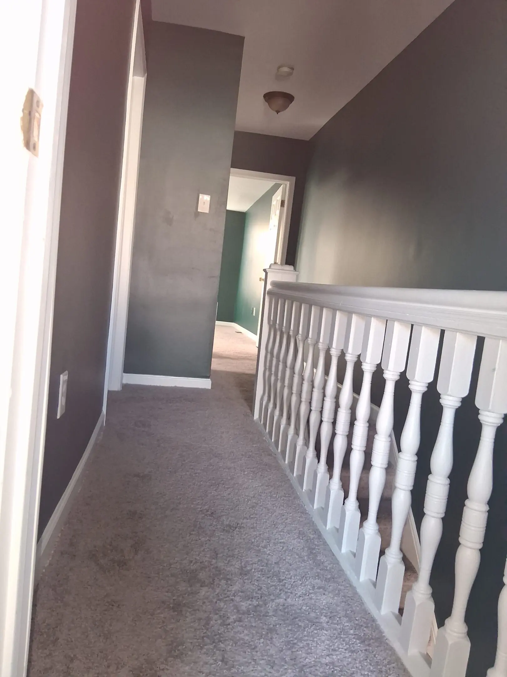 A carpeted hallway with white railing and gray walls.