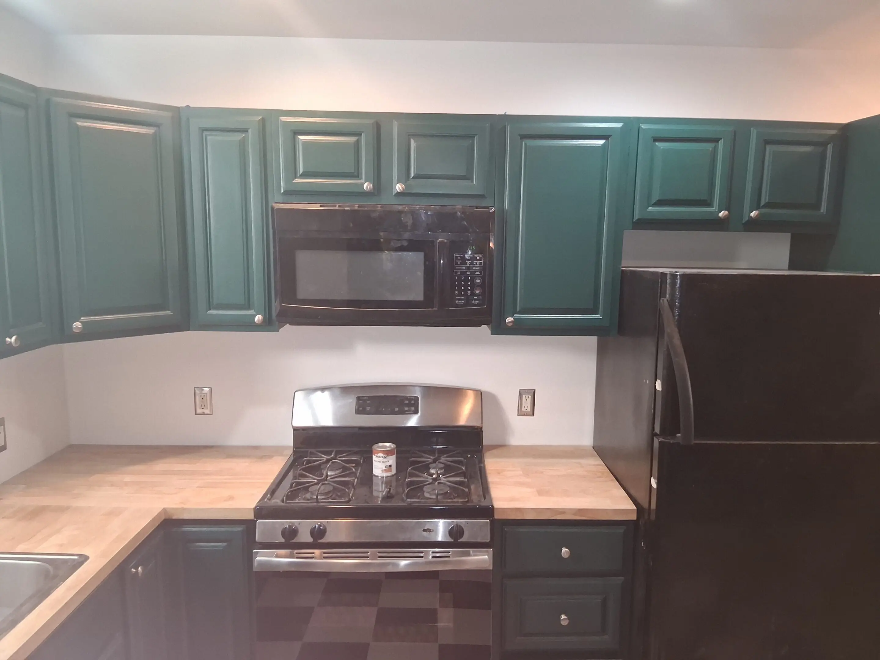 Modern kitchen with green cabinets and black appliances.