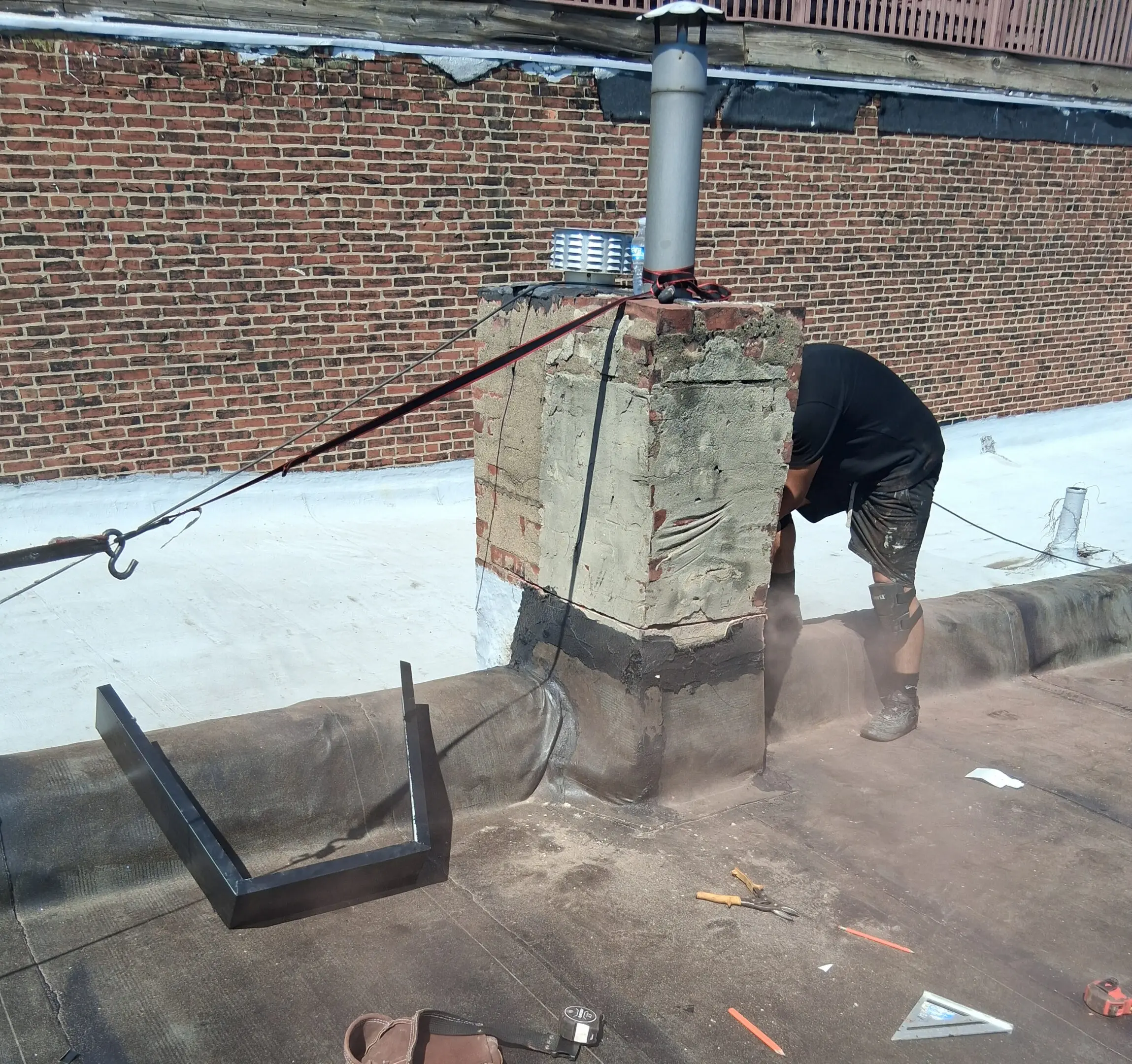 Person working on a rooftop near a chimney with tools scattered around.
