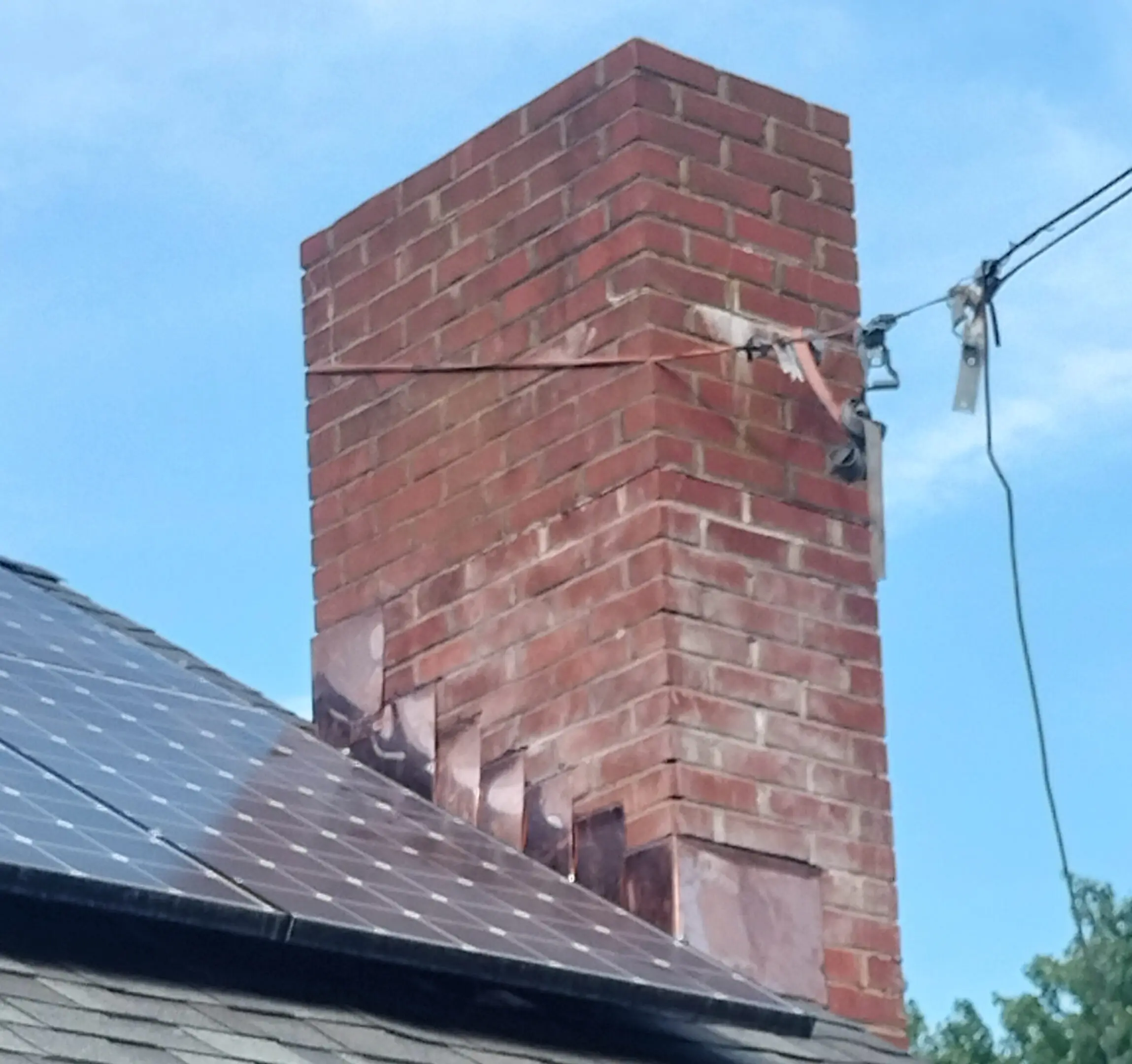 A tall red brick chimney with stairs on one side against a blue sky.