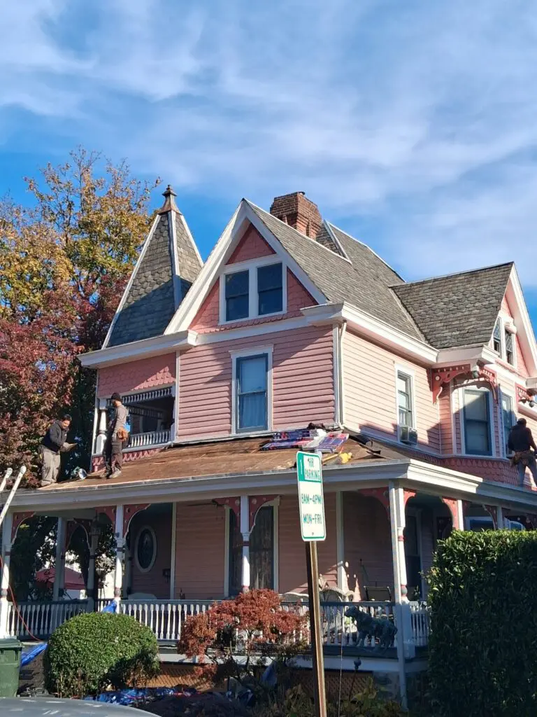 A charming pink Victorian house with a wrap-around porch under a clear blue sky.