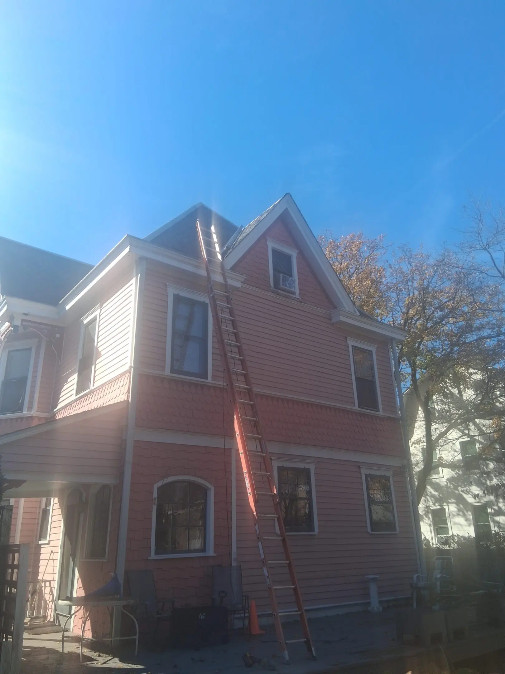 A two-story house with a ladder leaning against it on a sunny day.