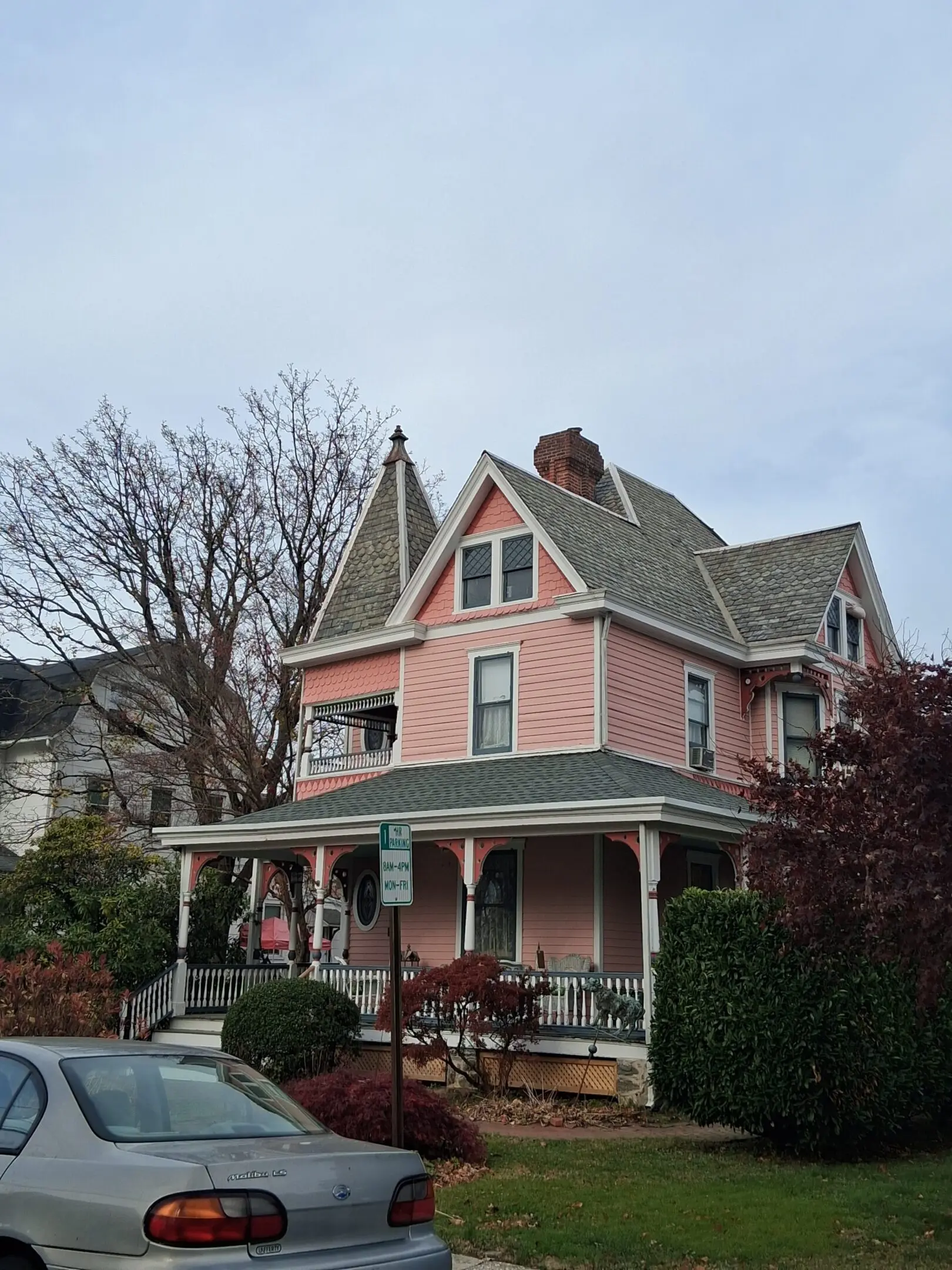A large pink Victorian house with a porch and bare trees.