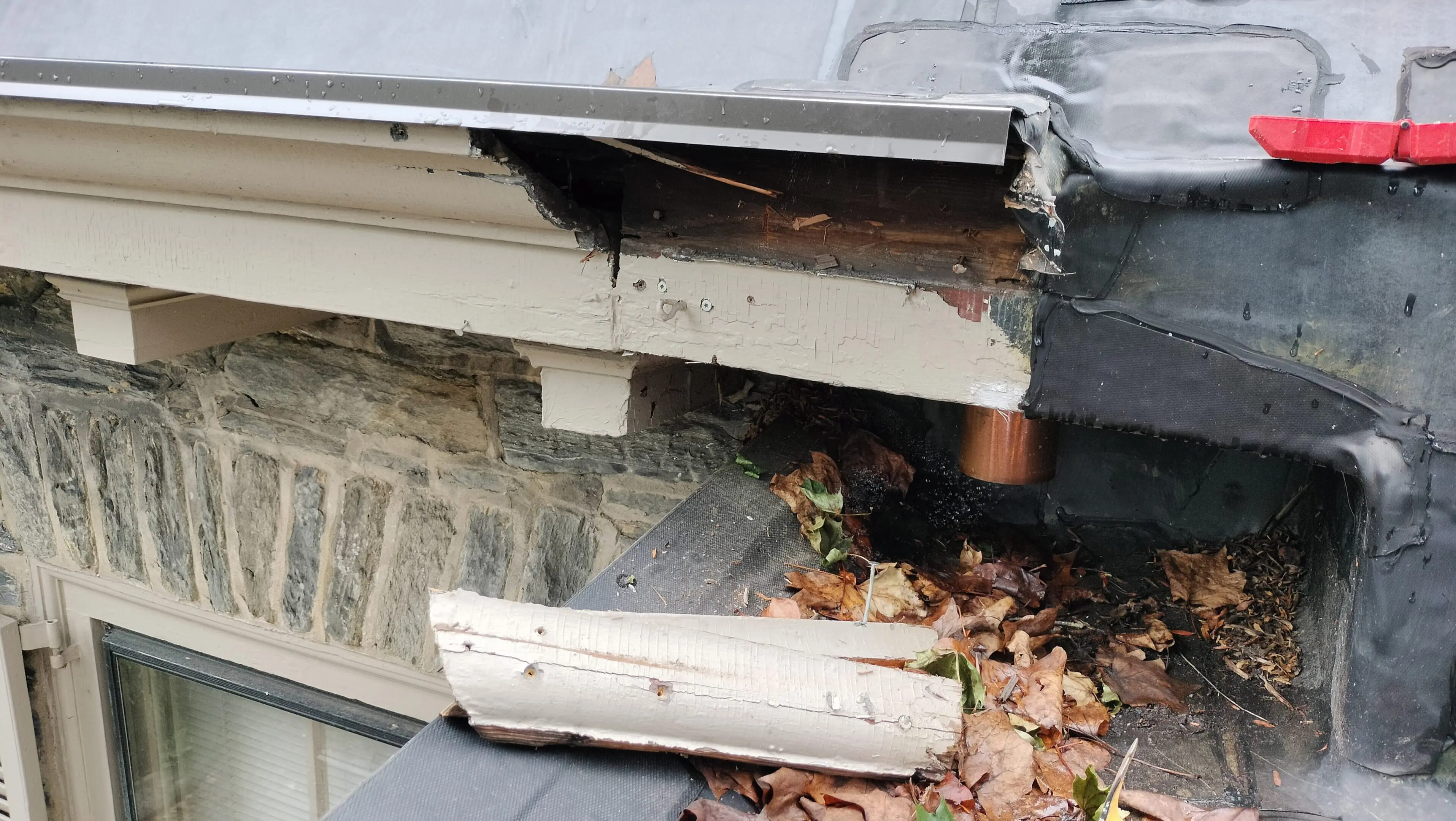 Damaged gutter section lying on the ground next to a house roof.