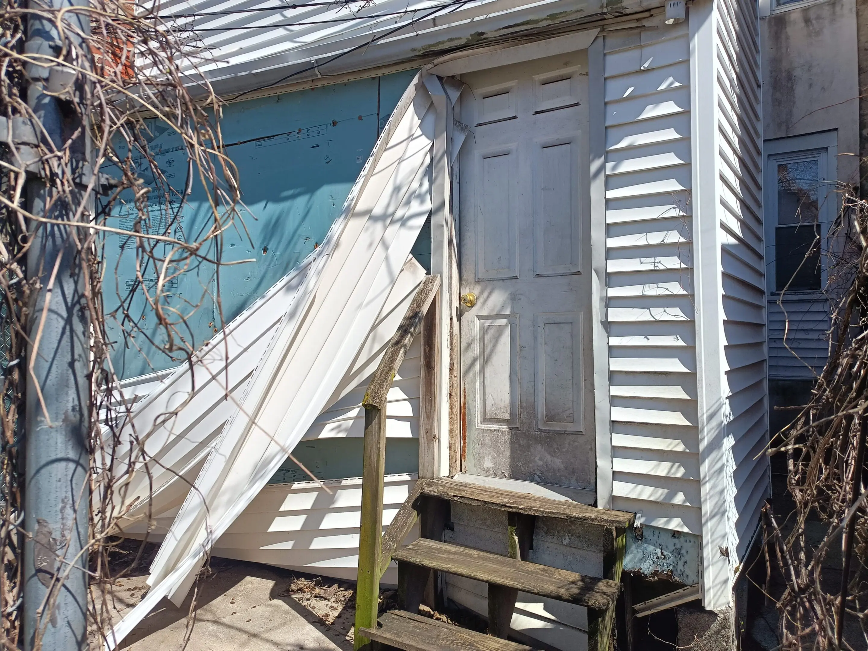 Old white wooden door with broken porch steps and torn tarp.