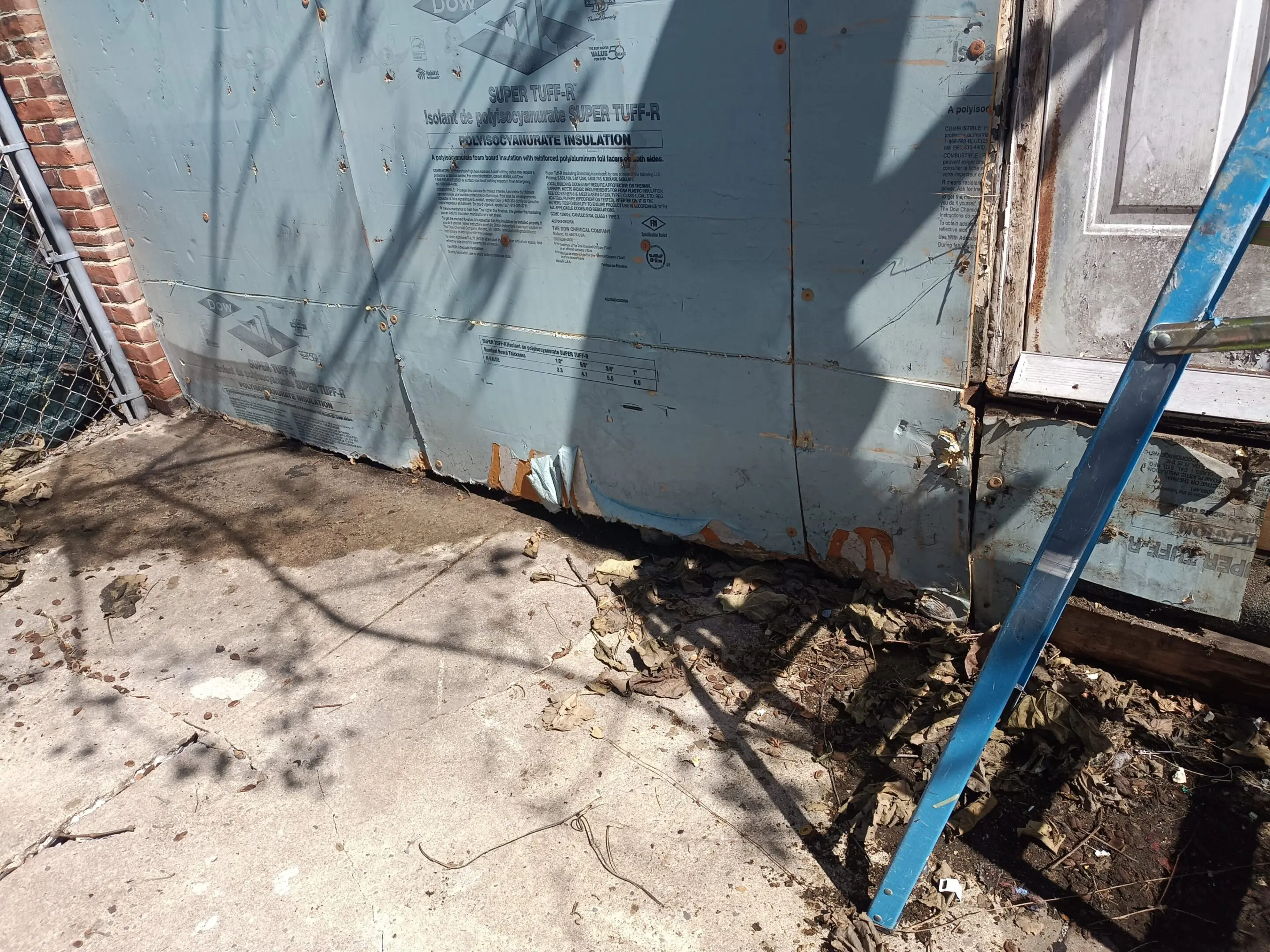 A blue metal container with a shadow and dry branches on the ground.