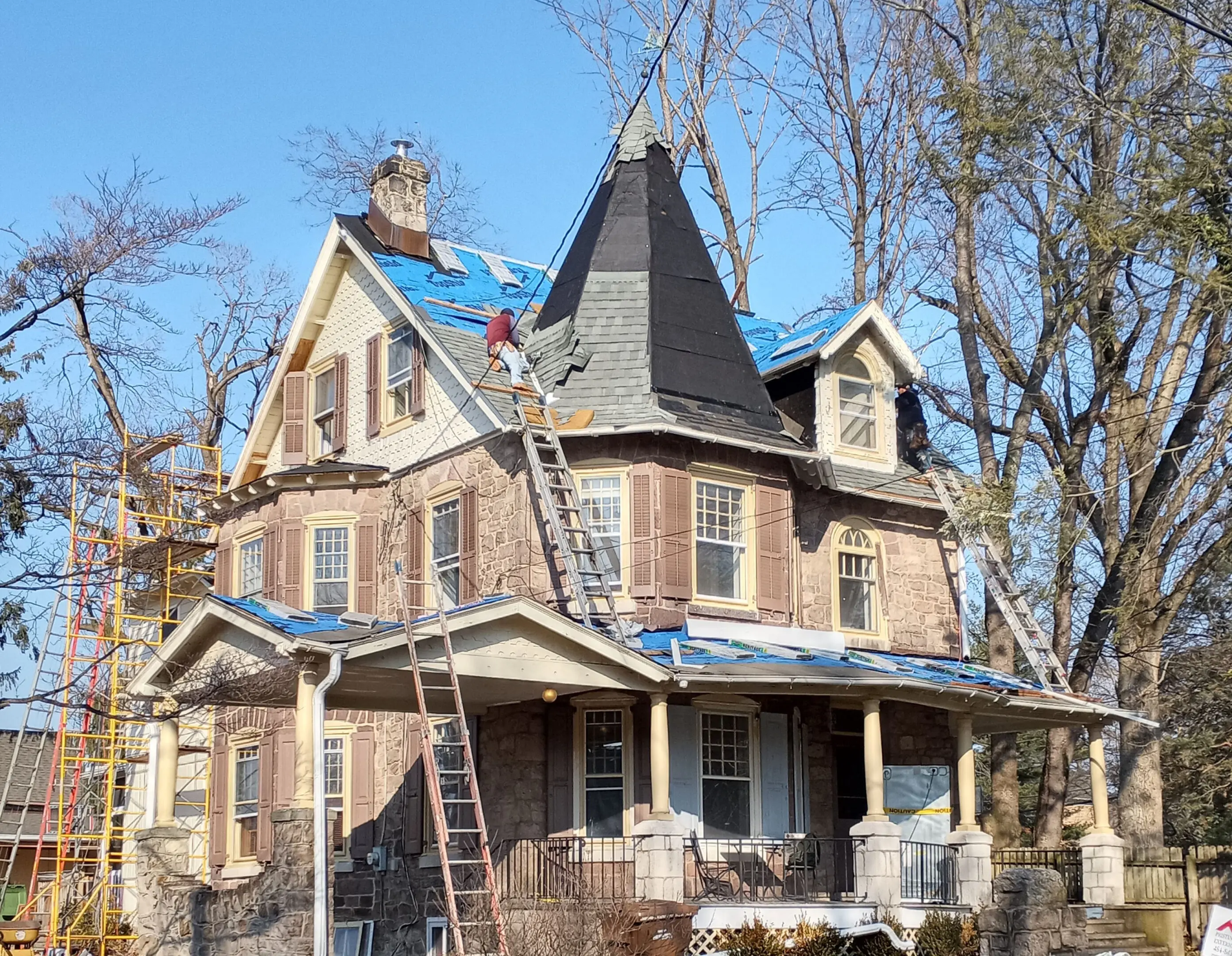 A Victorian-style house under renovation with workers on ladders.