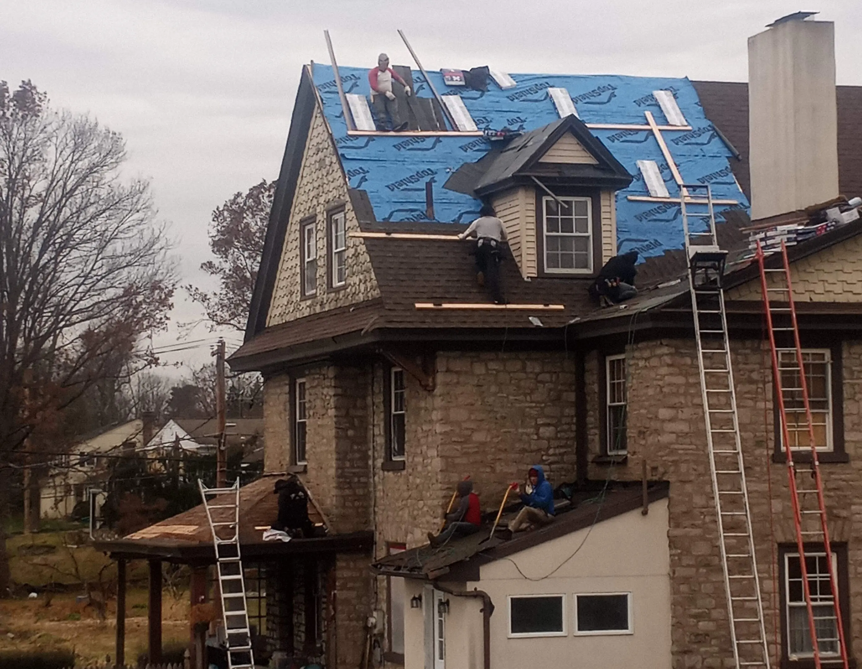 Workers installing blue roofing material on a house roof.