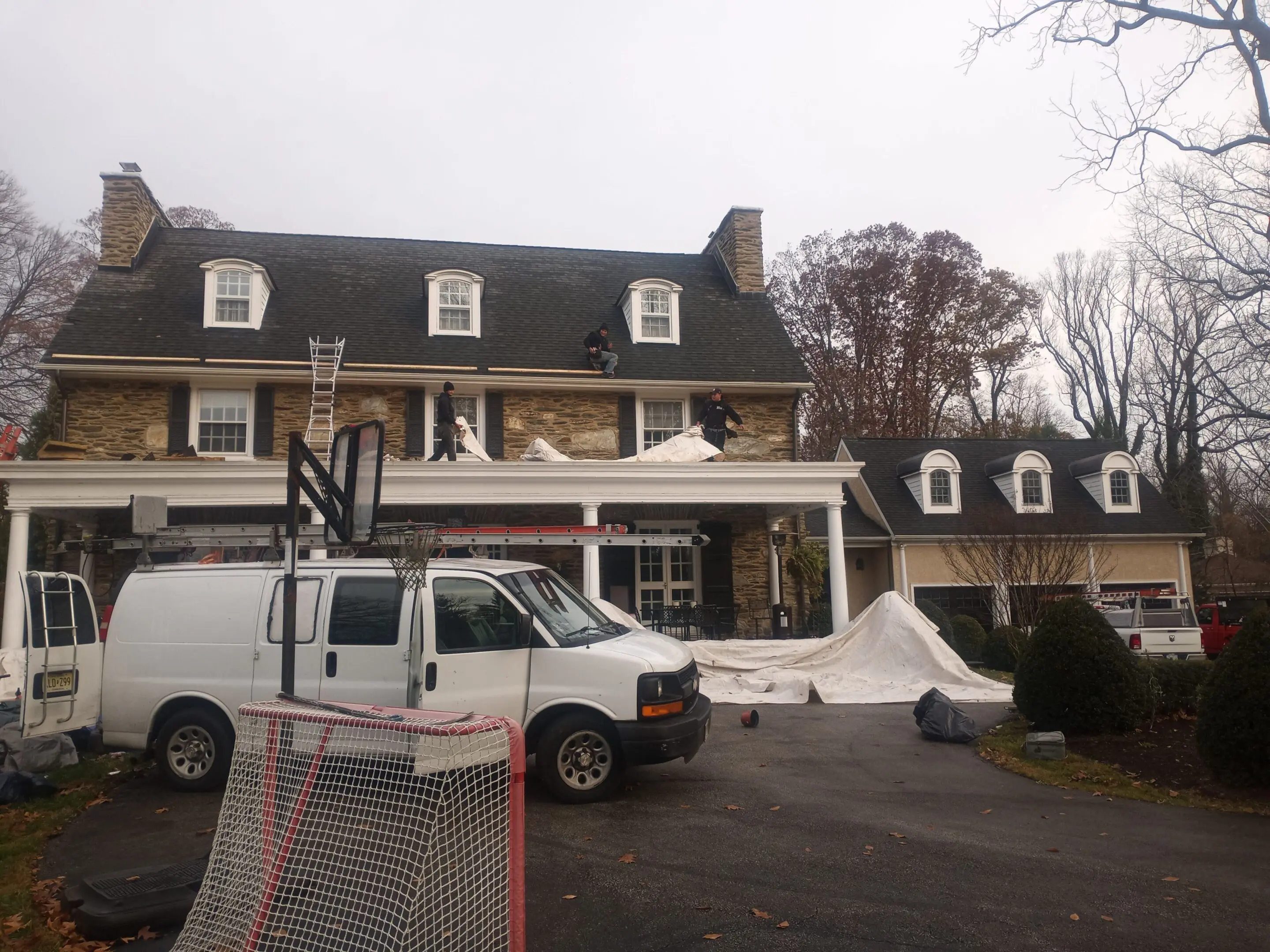 A large house with a white work van parked outside during roof work.