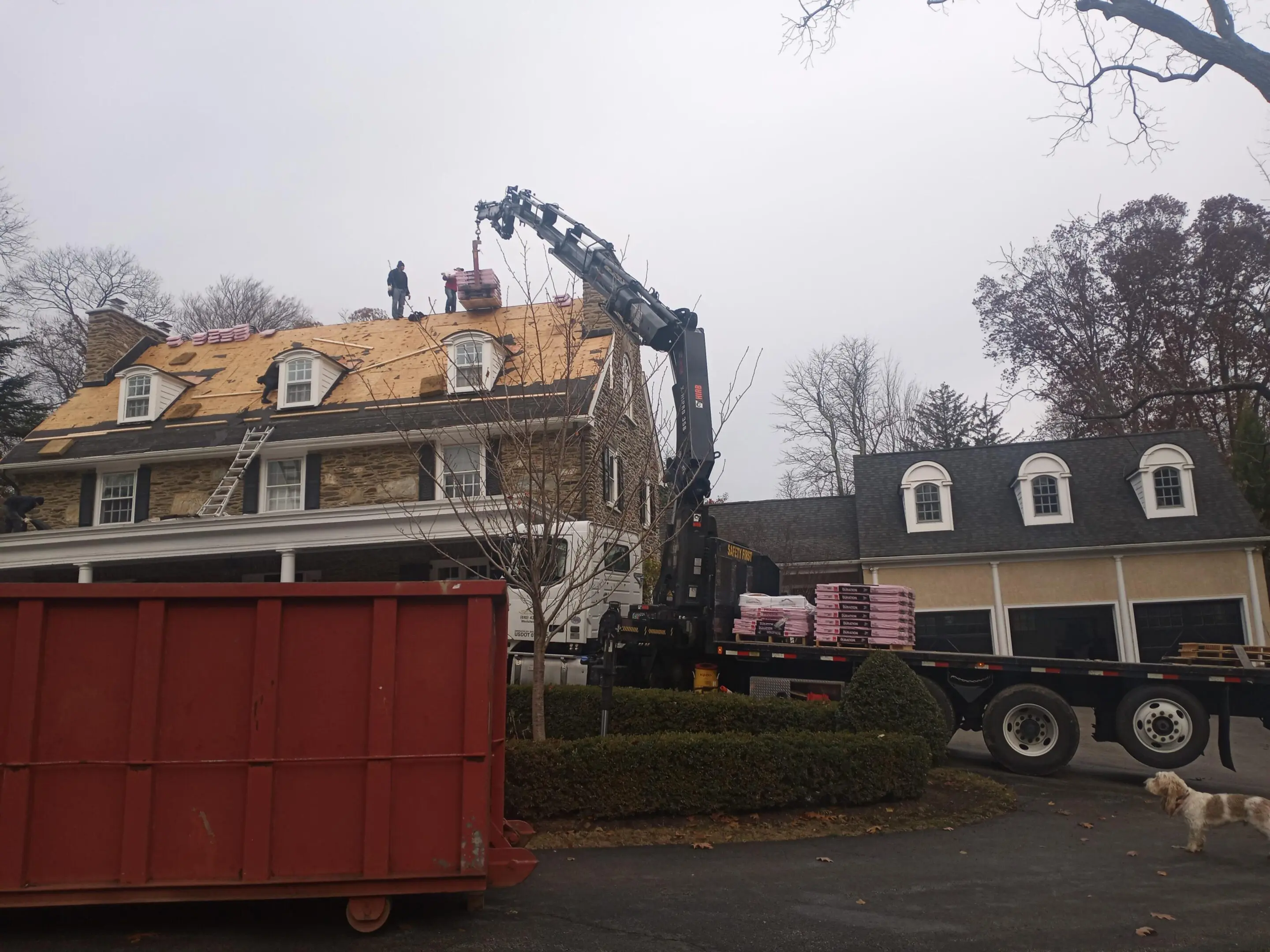 Workers repairing a roof using a crane on a cloudy day.