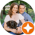 Couple smiling outdoors with their black dog in a park.